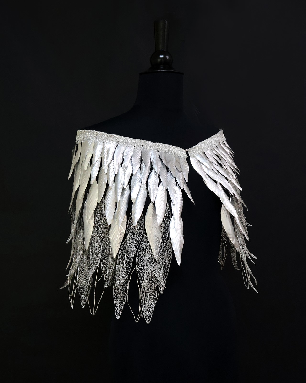 Ornys
Ornys se déploie comme une cape que l’on enfile, tel un pelage précieux. Les plumes, façonnées en métal argenté, composent un dégradé où la matière, habituellement dense, se fait aérienne. Plus le regard descend, plus les formes s’ouvrent, s’ajourent, laissant apparaître le vide comme une respiration.
Le métal devient plume, la rigidité devient légèreté. Cette pièce est une réinterprétation de la photographie "Qui es-tu, toi qui regardes ?" de @muriel_penicaud qui m'évoque un dos de plumes, une présence à la fois intime et insaisissable. Ornys est une parure légère, presque vivante, qui prolonge le mystère de l’image et invite à une métamorphose silencieuse. Broderie métallique et repoussé, cuivre argenté, aluminium et cannetille, 2026 . Avec le @collectif.qui.es.tu, nous avons créé une exposition itinérante mettant en lumière la richesse des métiers d’art.
Au Bastille Design Center, lors de l'exposition @de.main.de.maitre, organisé par la @cfma_metiersart , nous vous avons présenté le travail du collectif du 10 au 12 Avril.
De nouvelles dates d'expositions seront bientôt annoncées, avec de nouveaux artisans d'art qui rejoignent le projet ! .
.
.
.
.
.
#mariearchambaud #broderiemetallique #metal #argent #plumes #hautecouture