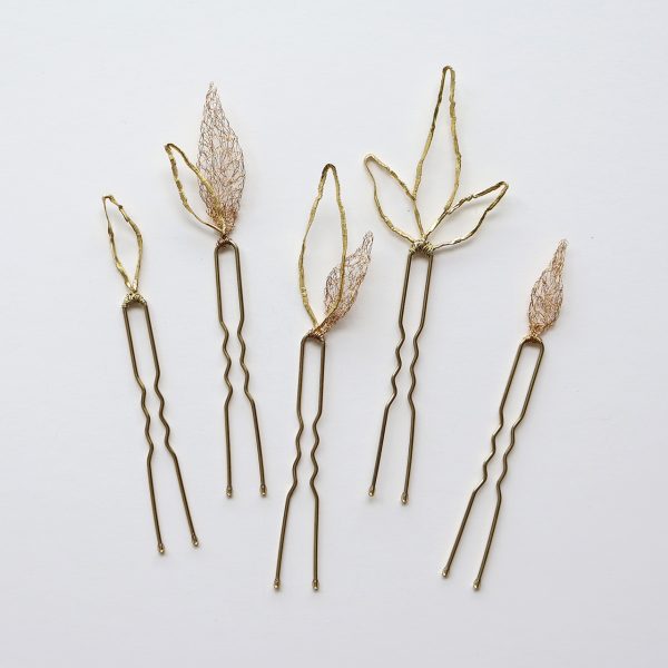 Lot de cinq pics à cheveux à intégrer dans des coiffures de mariage, réalisés à la main au fil de cuivre vernis à l'or. Ils représentent des feuilles légères et poétiques.