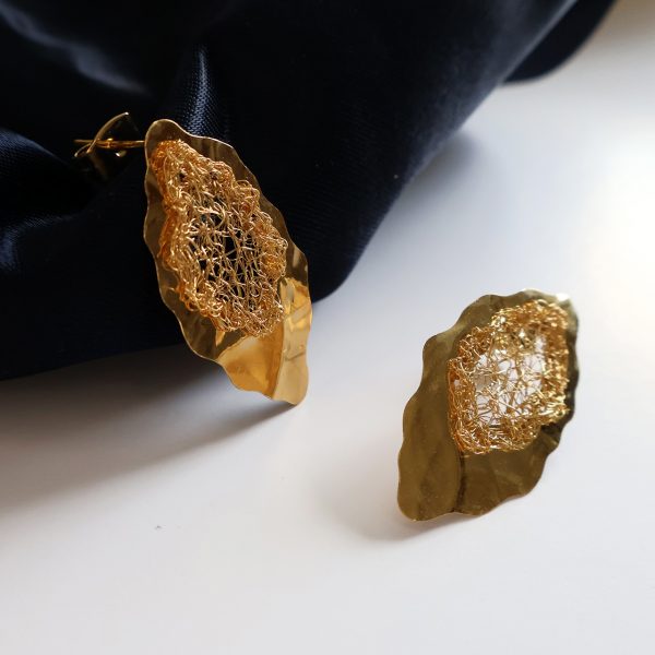 Les boucles d'oreilles Lobos 1 sont des bijoux uniques brodés à la main par la marque Marie Archambaud. Elles reposent délicatement sur un tissu bleu marine, mettant en valeur l'éclat doré du métal. Inspirées de la feuille de chêne, les boucles sont formées d'une plaque de métal texturée et de délicats fils brodés en leur centre.