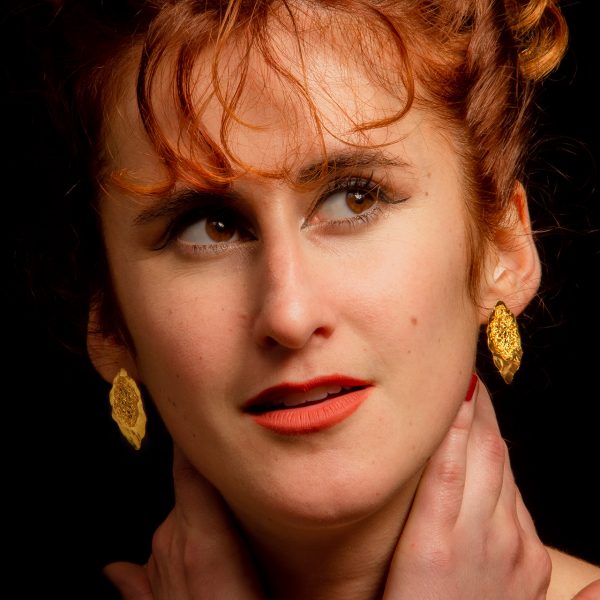 Une jeune femme rousse porte les boucles des boucles d'oreilles dorées de la marque Marie Archambaud