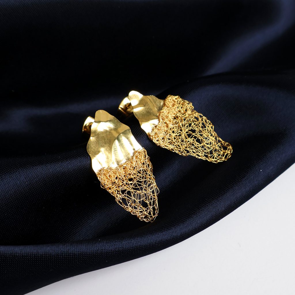 Boucles d'oreilles Lobos 2, bijoux uniques brodés à la main par la marque Marie Archambaud. Les boucles sont positionnées sur un tissu bleu marine faisant ressortir l'or du métal. Elles sont asymétriques et composées d'une plaque de métal texturée et de fil brodé fin.