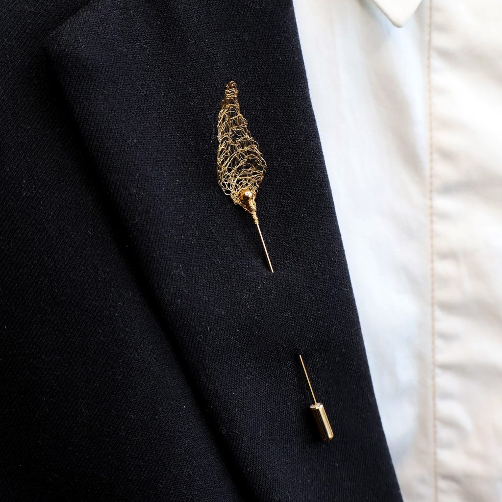 Boutonnière Aron piquée dans une veste. Feuille légère en fil dorée.