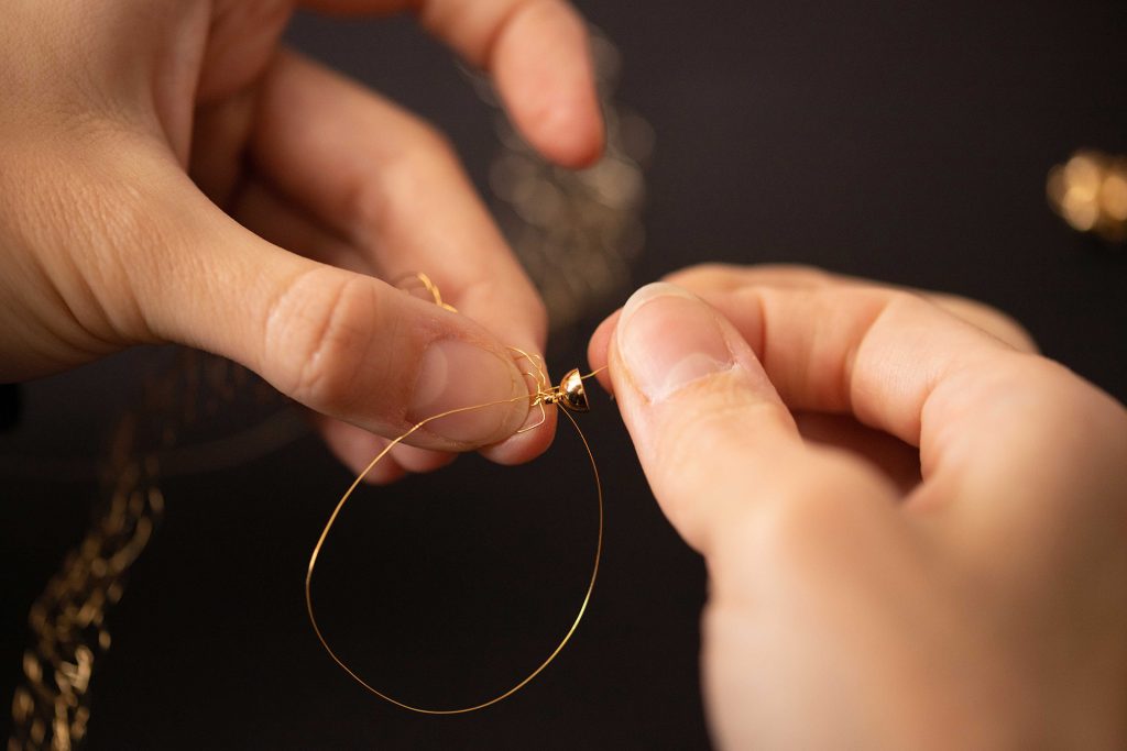 Deux mains cr&eacute;ant une boucle au fil m&eacute;tallique pour accrocher un fermoir sur le bracelet Lumio.