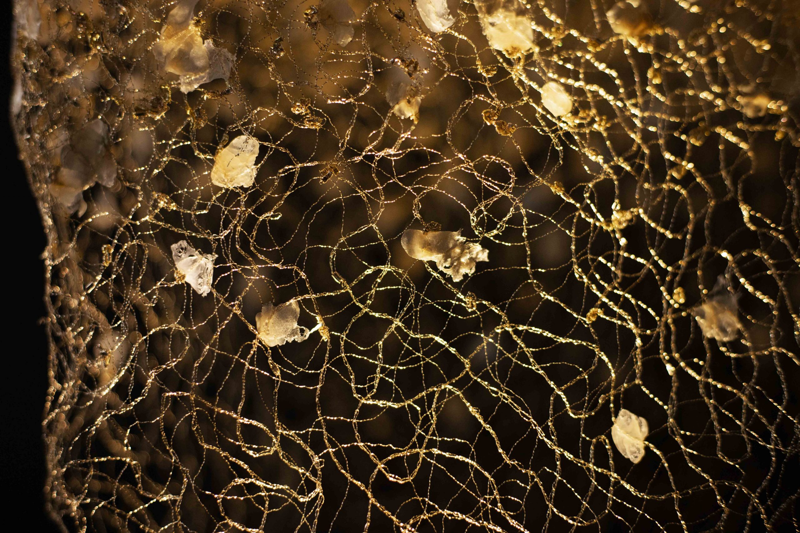 Détails de broderie métallique du bijou-vêtement Envol, conçu par la créatrice Marie Archambaud. On aperçoit le réseau de fils de cuivre vernis à l'or captant la lumière et les pétales de pastique.