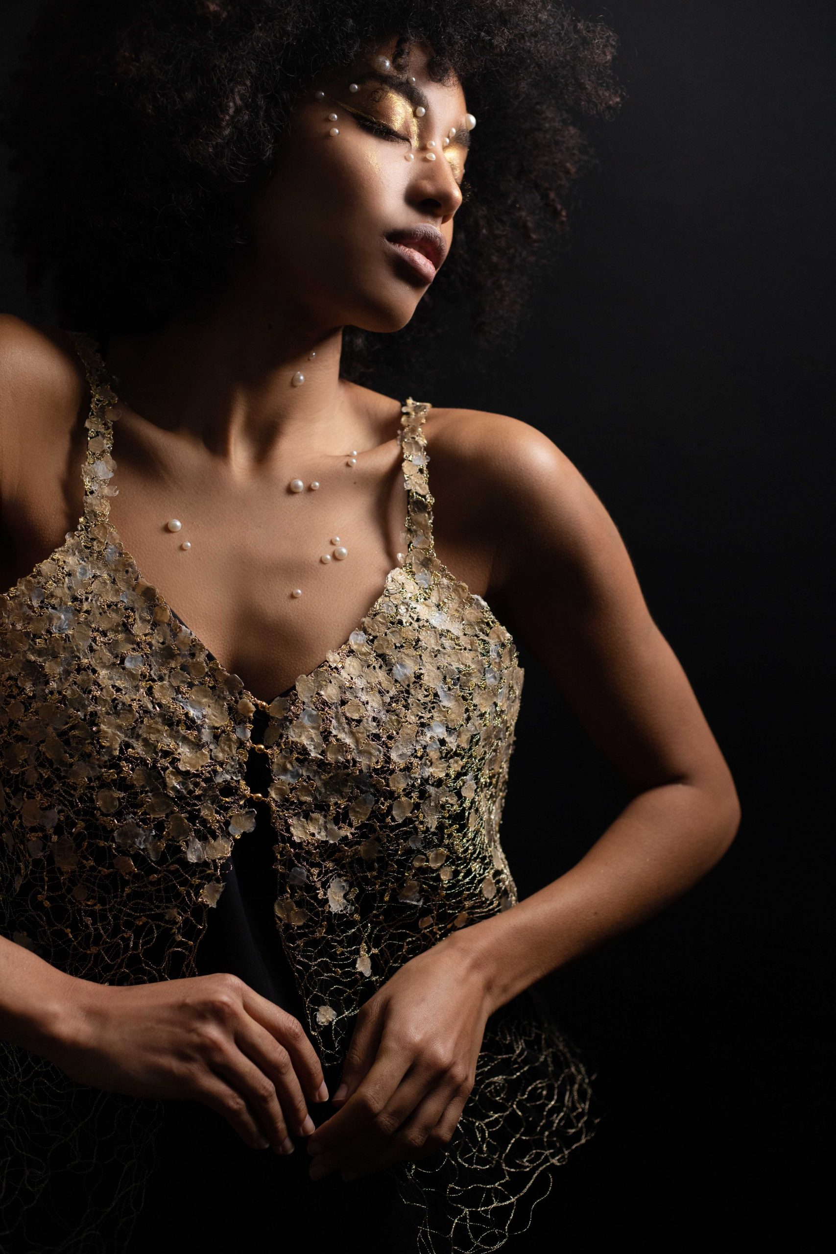 Jeune femme portant le bijou-vêtement Envol par dessus une robe à bretelles noires. Le top brodé est en parfaite superposition à la robe noire permettant ainsi de faire ressortir la broderie au fil d'or.