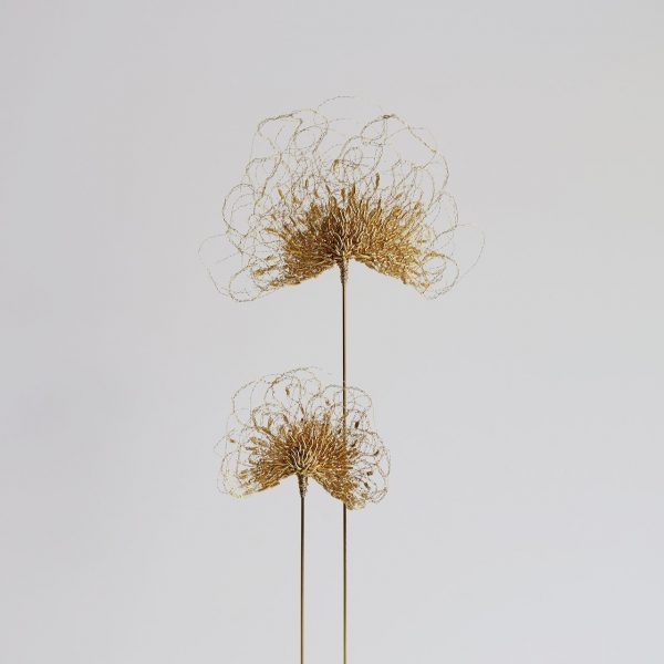 Détails de la sculpture Aurora sur fond gris. Deux tiges de laiton sont surmontées de feuilles brodées au fil d'or.