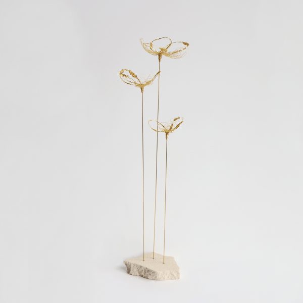 Sculpture Coccum sur fond gris. Trois tiges métalliques surmontées de fleurs brodées au fil d'or et piquées sur pierre de tufeau.