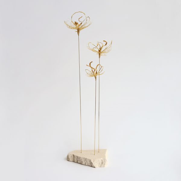 Sculpture Iridis sur fond gris. Trois tiges métalliques surmontées de fleurs brodées au fil d'or et piquées sur pierre de tufeau.