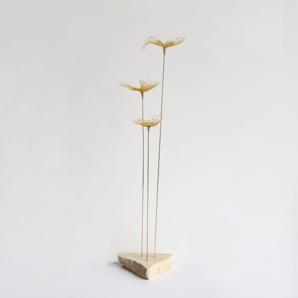 Sculpture Trifo sur fond gris. Trois tiges métalliques surmontées de fleurs brodées au fil d'or et piquées sur pierre de tufeau.