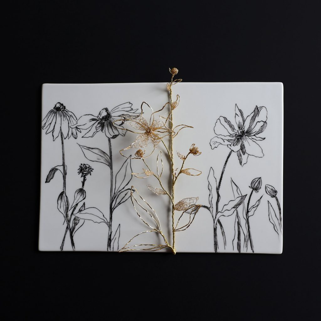 Tableau de porcelaine blanche sur fond noir. Fleurs peintes en noir et brodées en trois dimensions au fil d'or.