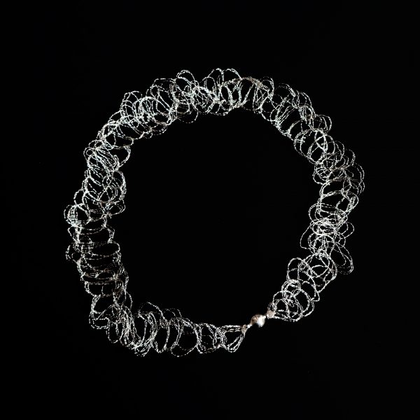Collier ras de cou Lumi argenté sur fond noir. Il est réalisé à la main par une technique de maille métallique propre à l'atelier Marie Archambaud.