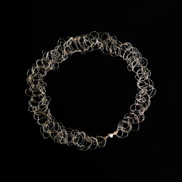 Collier ras de cou Lumi or champagne sur fond noir. Il est réalisé à la main par une technique de maille métallique propre à l'atelier Marie Archambaud.