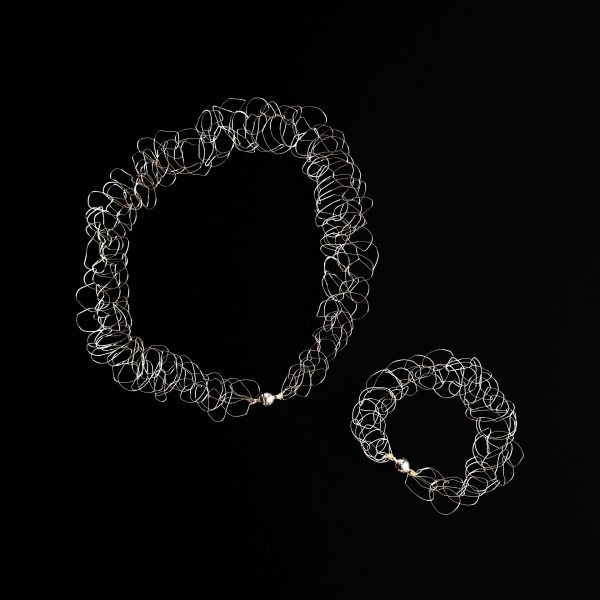 Collier et bracelet au fil d'argent sur fond noir faisant ressortir les détails de la maille