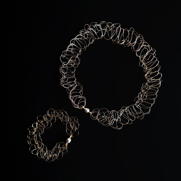 Collier et bracelet au fil doré clair sur fond noir faisant ressortir les détails de la maille.