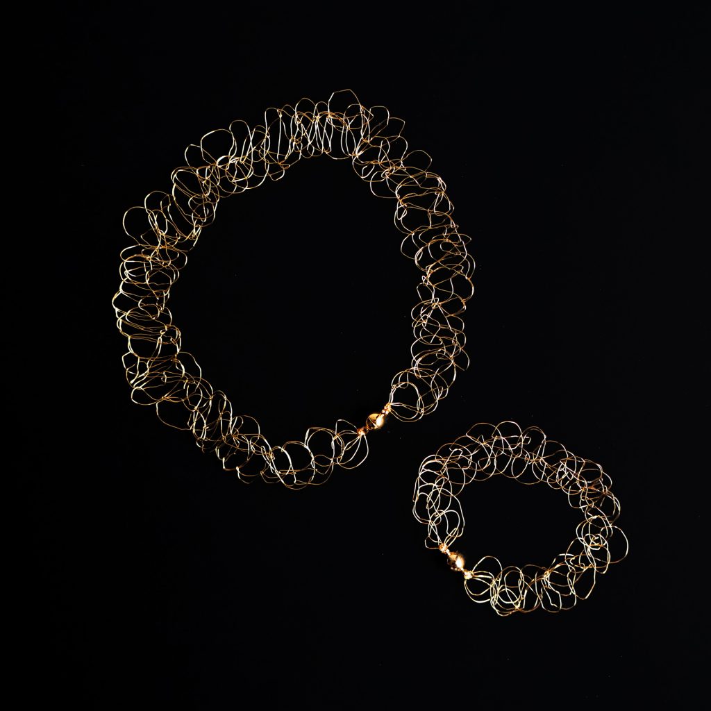 Collier et bracelet au fil doré sur fond noir faisant ressortir les détails de la maille.