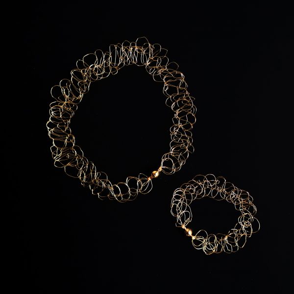 Collier et bracelet au fil doré sur fond noir faisant ressortir les détails de la maille.
